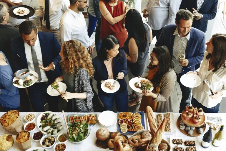 Ludzie na imprezie firmowej stojący przy stole z cateringiem